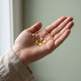 Two small golden-yellow softgel capsules resting in the palm of a person's hand, with a neutral, soft-focus background.